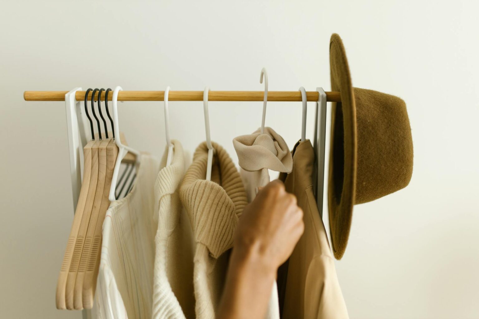 Clean, organized closet with neutral colored clothing hanging neatly on wooden hangers