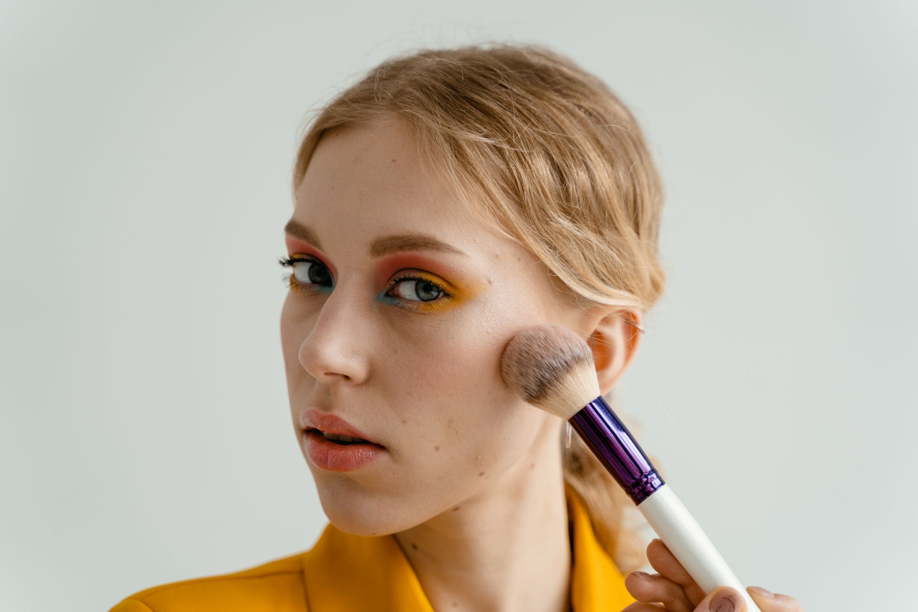 Woman applying cream bronzer stick to cheekbones in natural light